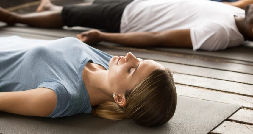 Group of young sporty people practicing yoga lesson lying in Dead Body or Corpse pose, Savasana exercise, working out, resting after practice, indoor close up, studio. Healthy lifestyle concept